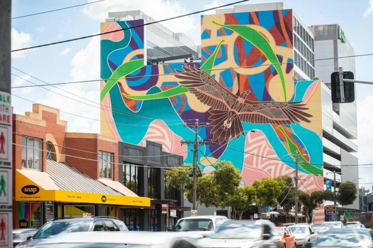 A large Indigenous mural featuring Bunjil on a building facade with cars in foreground